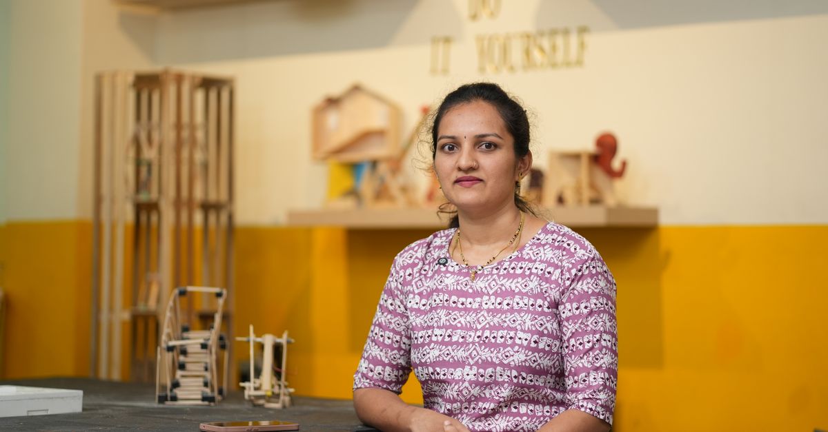 Woman sitting in a DIY workshop surrounded by wooden craft projects.